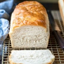 Loaf of white bread with a slice cut laying in front of it
