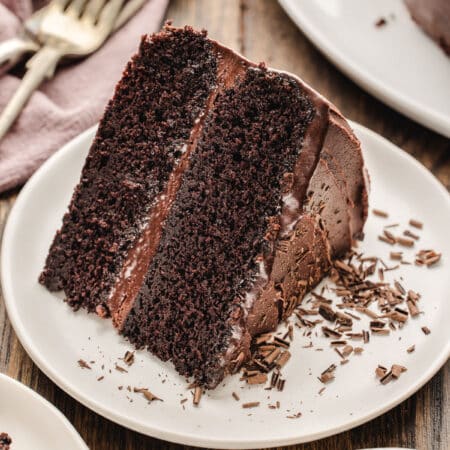 A slice of chocolate fudge cake with chocolate shavings on it.