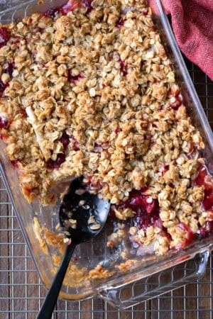 A black spoon in a dish of cranberry apple crisp.