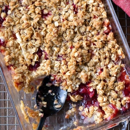 A black spoon in a dish of cranberry apple crisp.