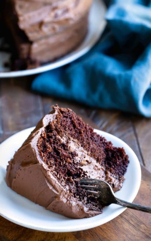 Slice of chocolate fudge cake on a white plate with a fork in it