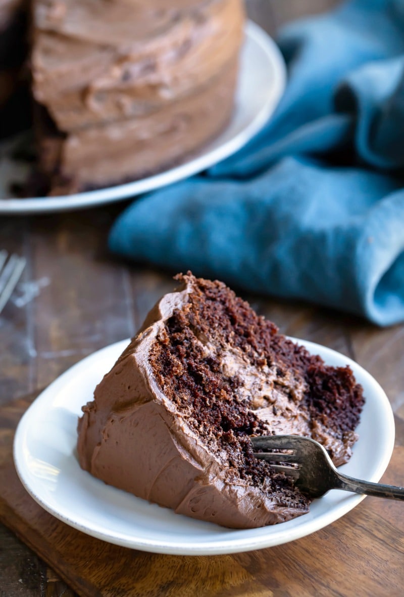 Slice of chocolate cake on a white plate next to a blue linen napkin