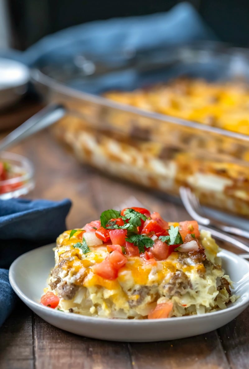 Piece of sausage breakfast casserole on a white plate next to a blue linen napkin