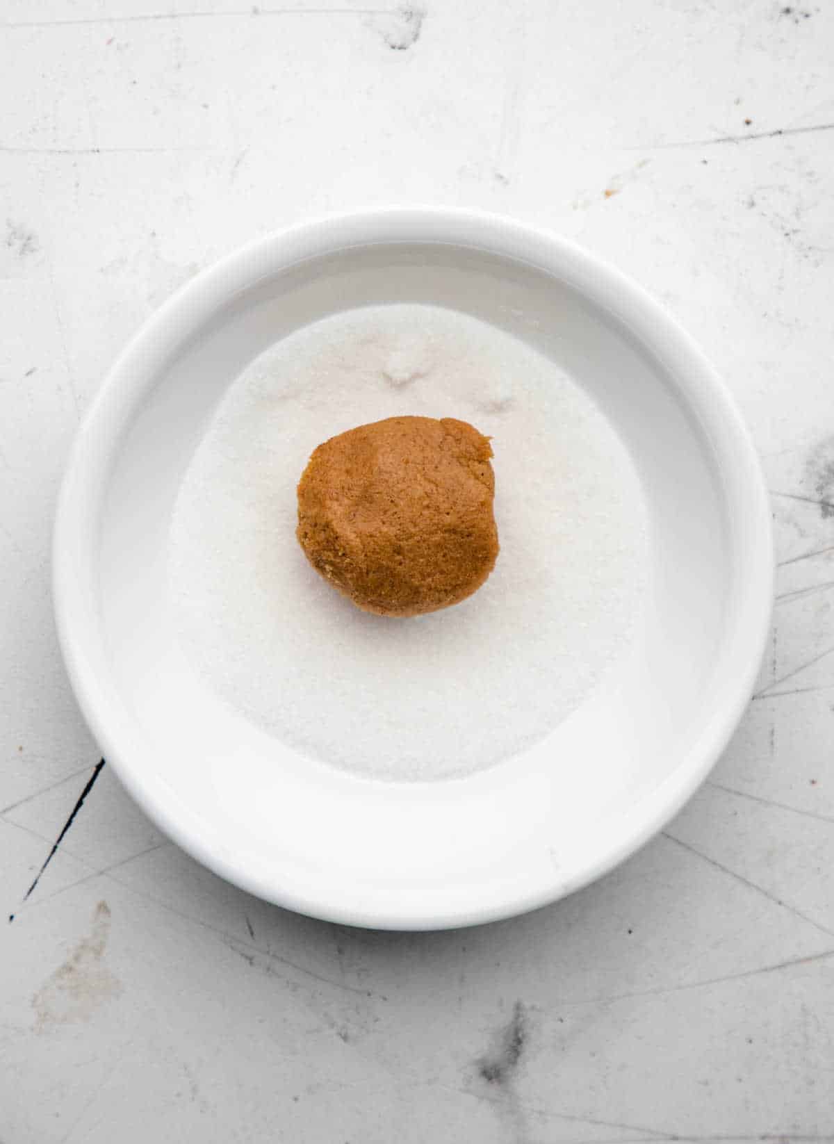 A molasses cookie dough ball in granulated sugar. 