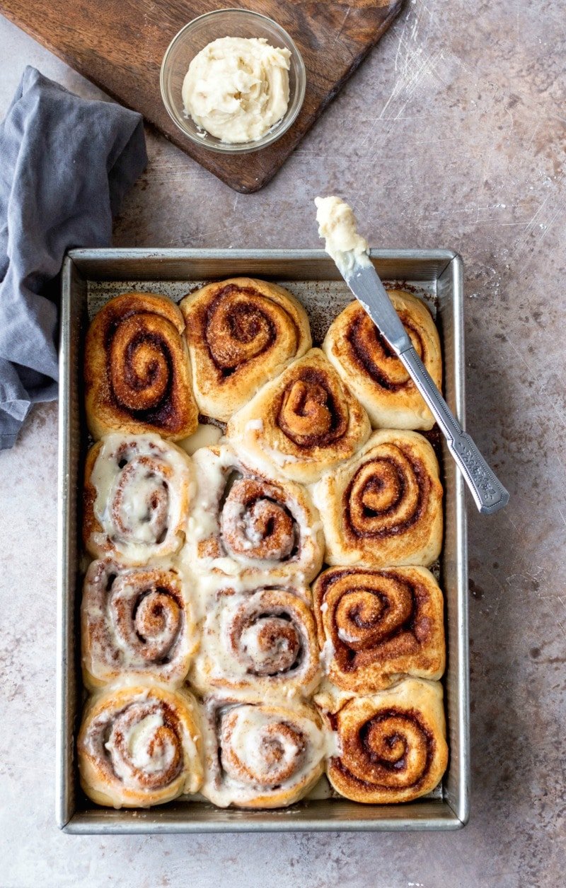 Pan of maple cinnamon rolls next to a dish of maple frosting