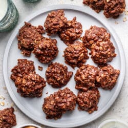 A plate of no bake cookies next to glasses of milk and a dish of peanut butter.