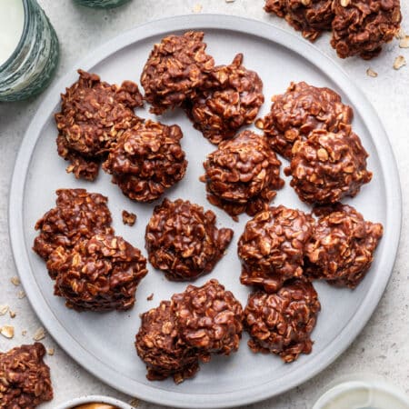 A plate of no bake cookies next to glasses of milk and a dish of peanut butter.