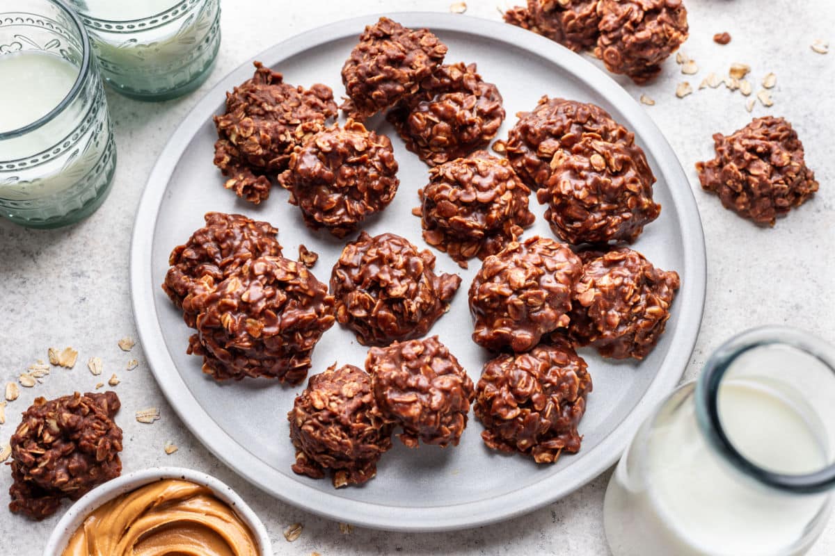 A plate of no bake cookies next to glasses of milk.