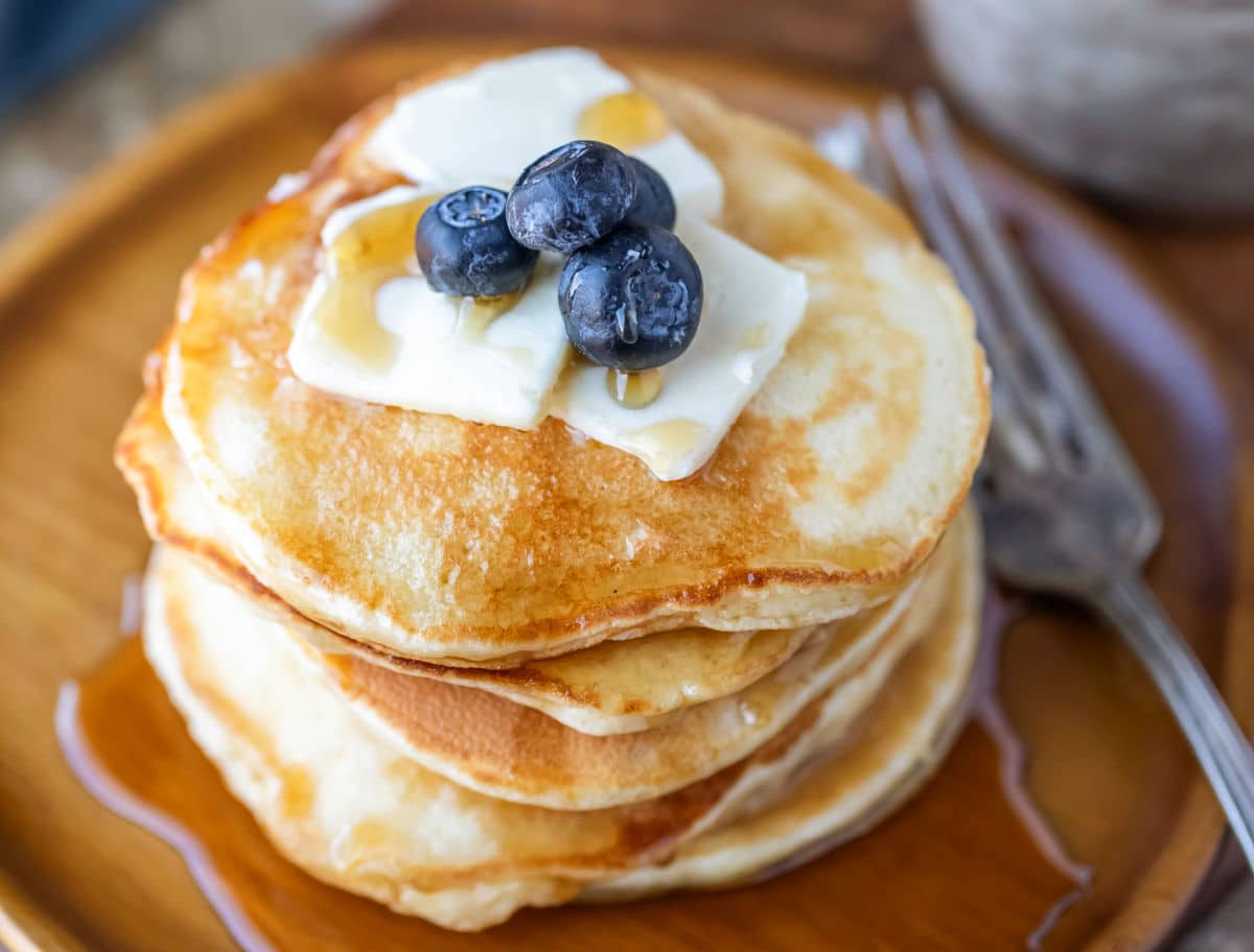 Sour Cream Pancake Recipe A stack of sour cream pancakes topped with syrup and butter pats.