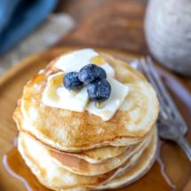 Stack of sour cream pancakes topped with butter syrup and blueberries