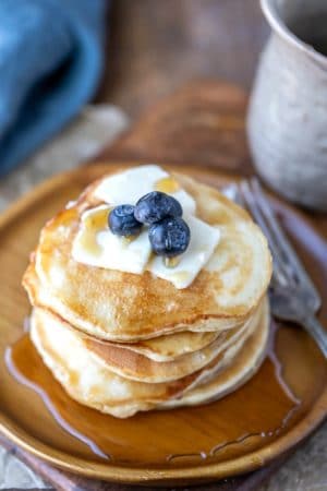 Stack of sour cream pancakes topped with butter syrup and blueberries