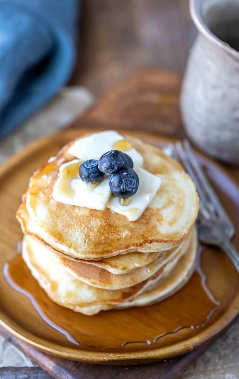 Stack of sour cream pancakes topped with butter syrup and blueberries