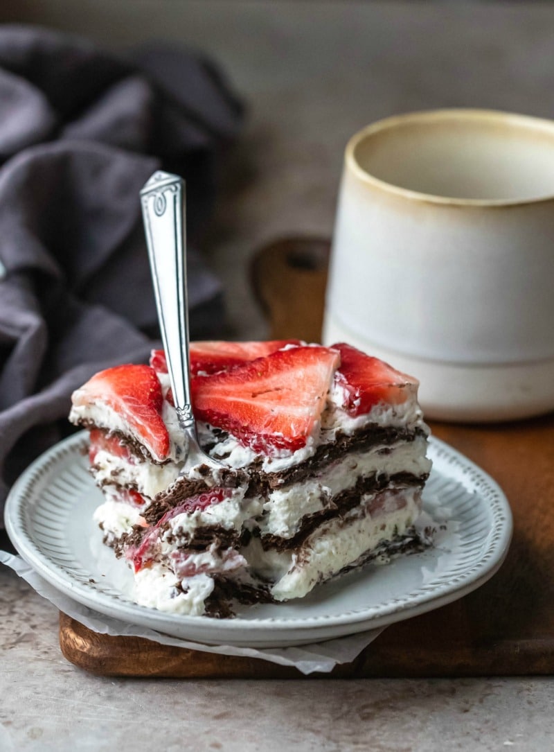 Slice of strawberry icebox cake next to a cream mug
