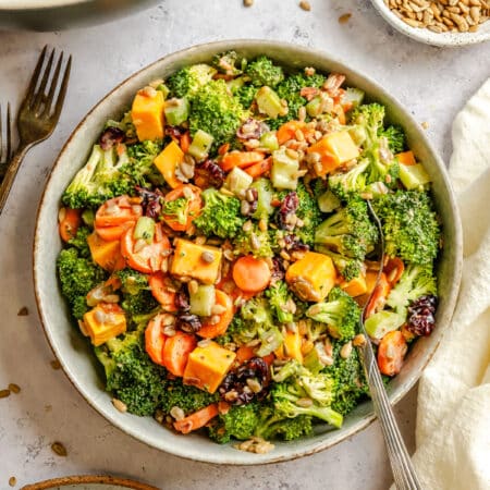 A bowl of broccoli salad next to a dish of sunflower seeds.