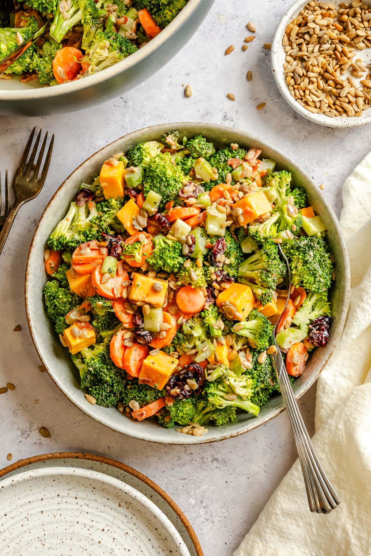 A bowl of broccoli salad next to a dish of sunflower seeds.