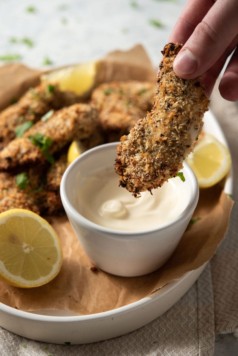 Someone dipping baked chicken tenders into a dipping sauce