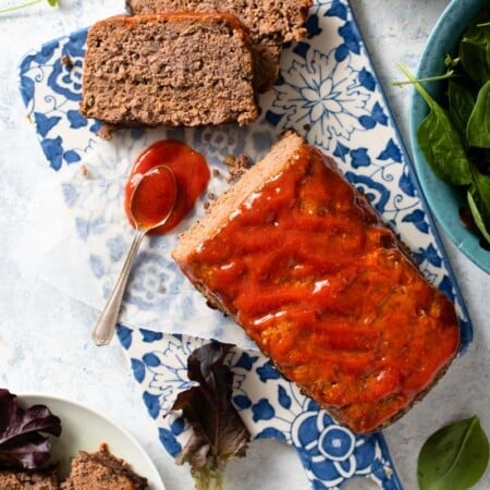 A meatloaf with two pieces cut next to a bowl of sauce.