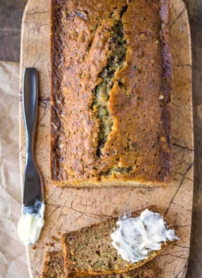 Loaf of zucchini bread with a slice cut and partially buttered.