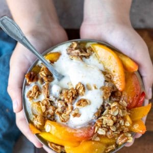 Hands holding a dish of skillet peach crisp