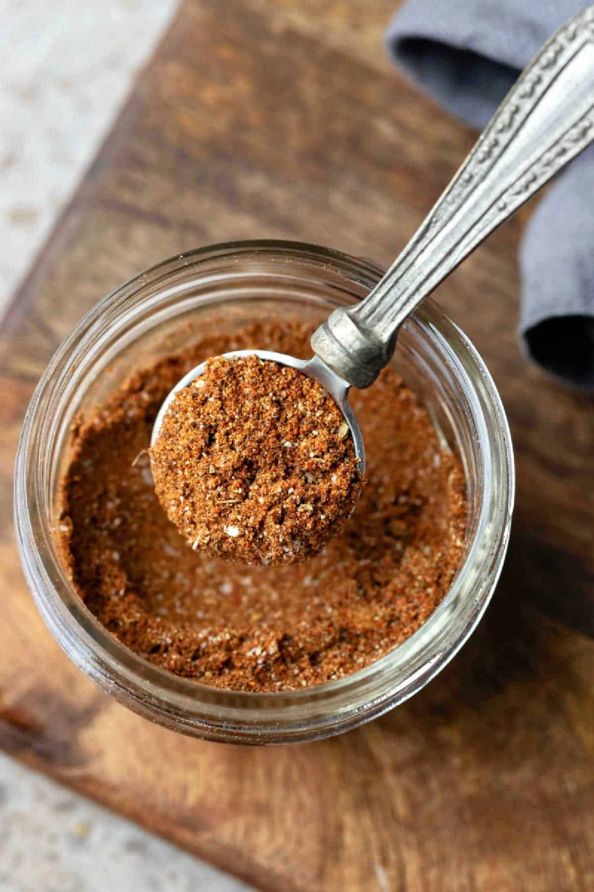 A silver measuring spoon in a glass jar of taco seasoning.