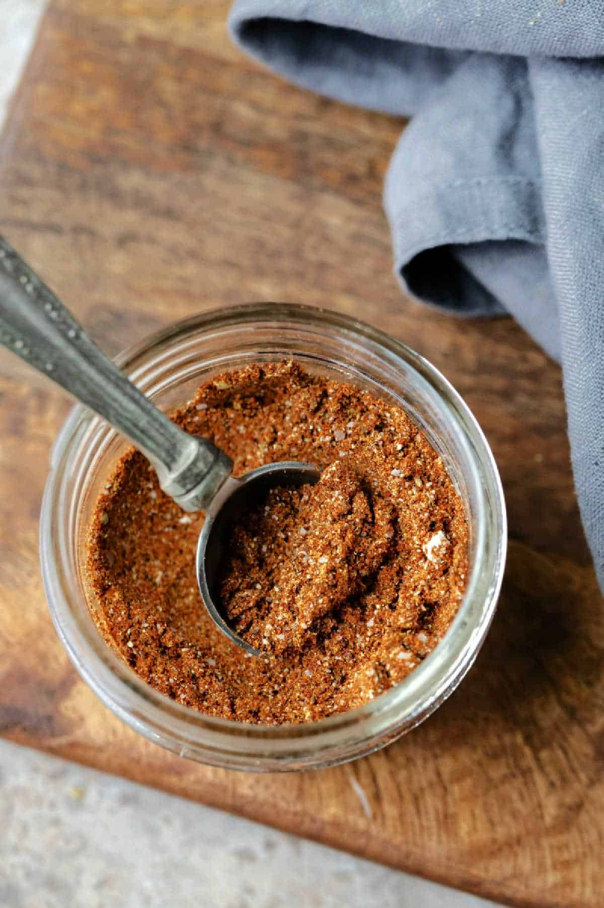 A glass jar of taco seasoning on a wooden cutting board. 