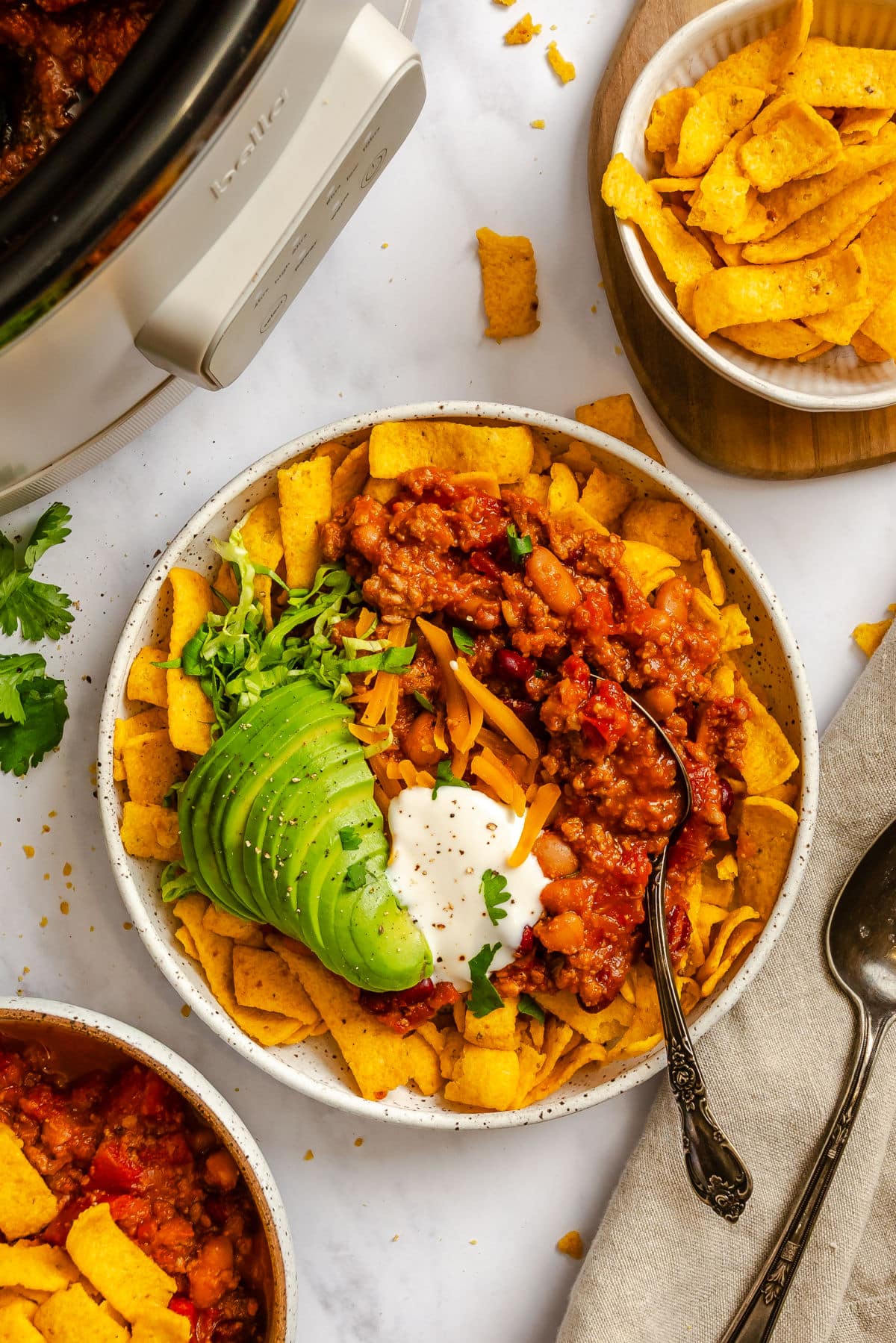 A dish of frito chili pie topped with sour cream and sliced avocado.