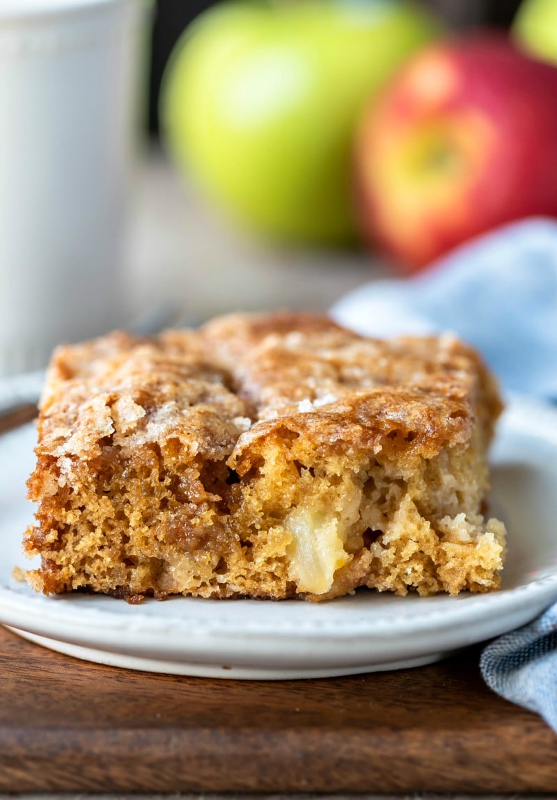 Slice of cinnamon apple cake next to red and green apples