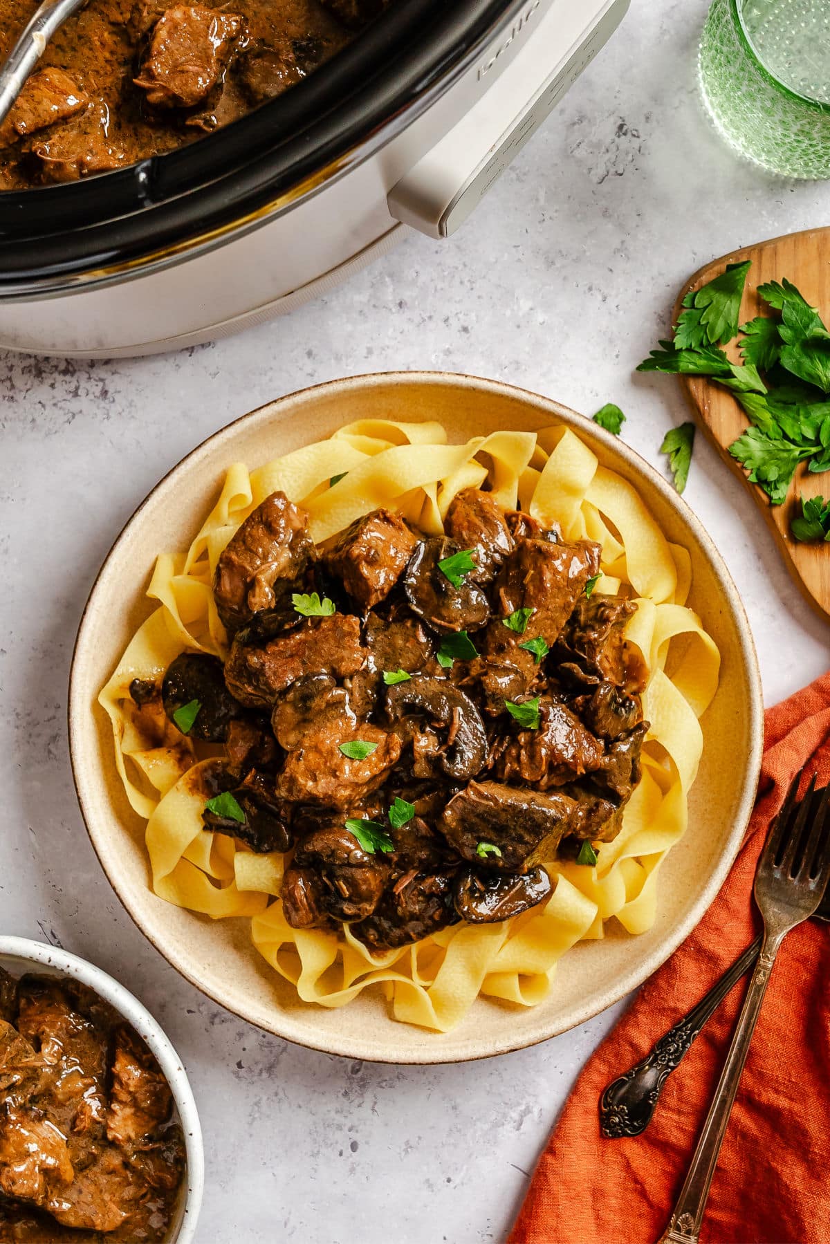 A plate of crock pot beef tips on egg noodles next to the crock pot.