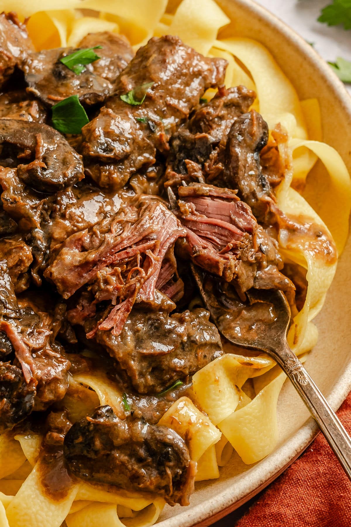 A fork with a bite of crock pot beef tips on it on egg noodles.