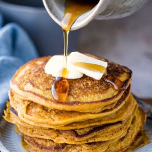 Crock of maple syrup pouring onto stack of pumpkin pancakes