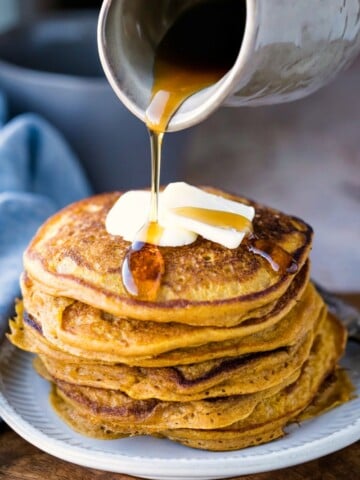 Crock of maple syrup pouring onto stack of pumpkin pancakes