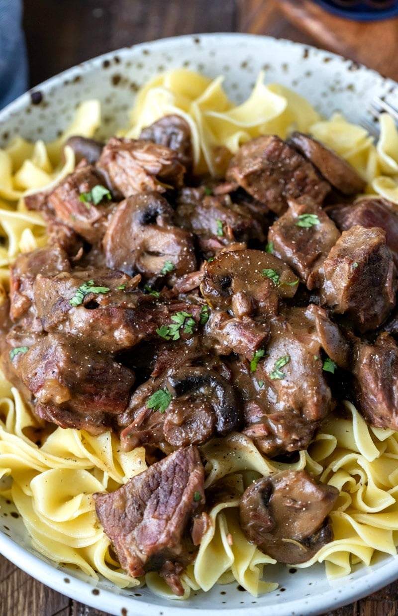 Closeup of crockpot beef tips with gravy over egg noodles