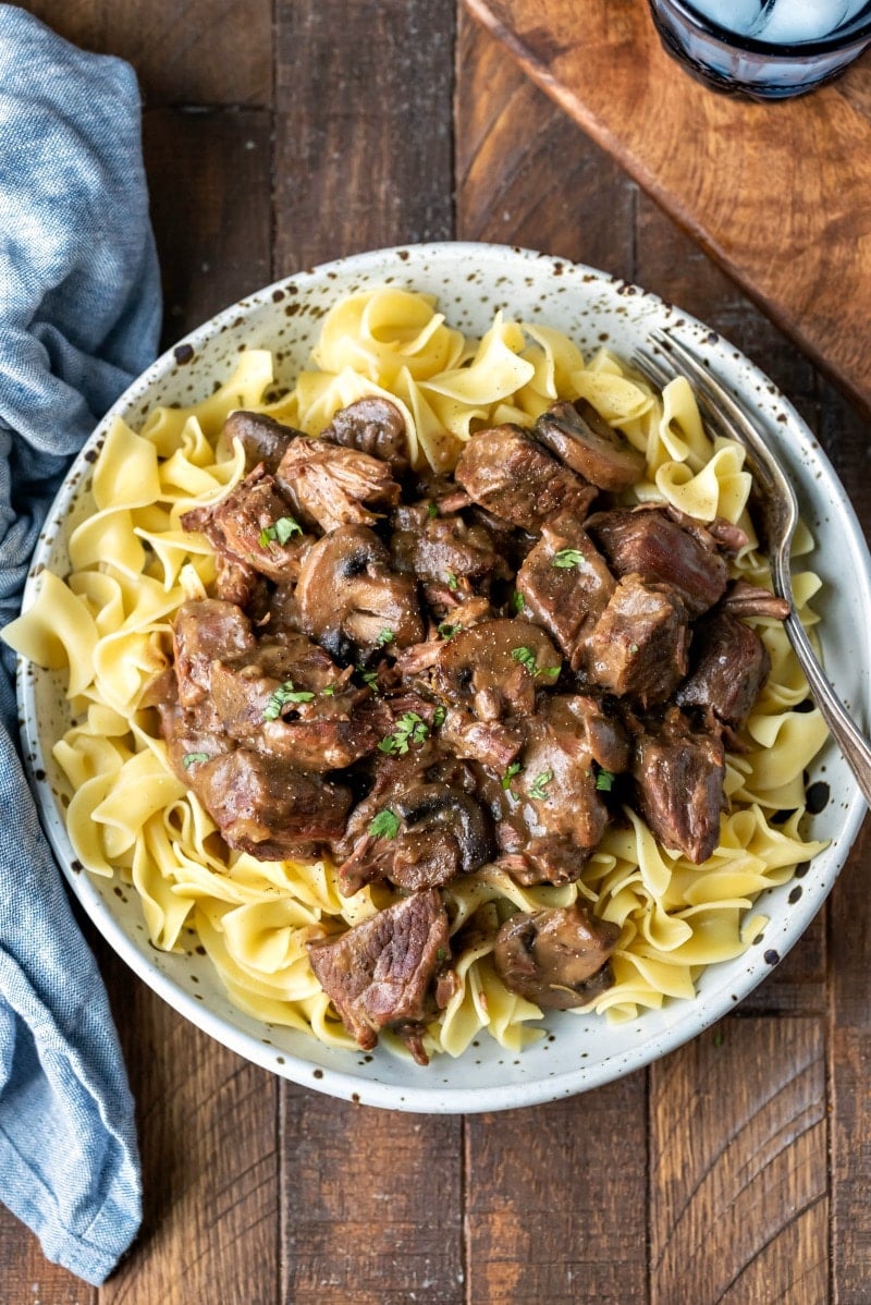 Crockpot beef tips over egg noodles on a speckled plate