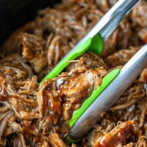 Green tongs picking up crockpot pulled pork