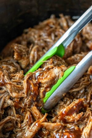 Green tongs picking up crockpot pulled pork