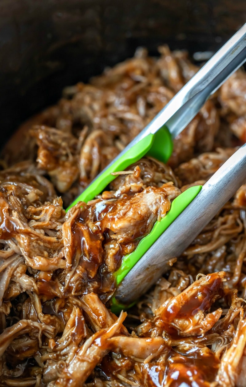 Green tongs picking up crockpot pulled pork