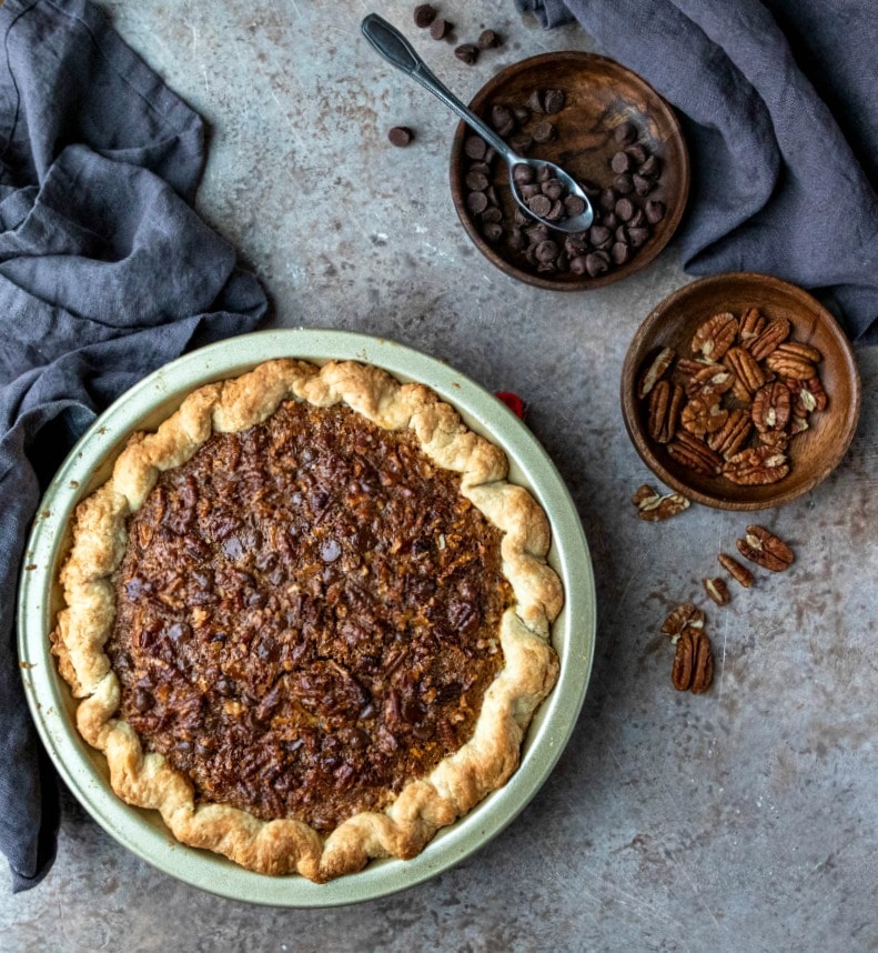 Chocolate pecan pie next to dishes of pecans and chocolate chips