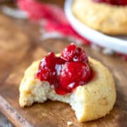 Cherry cheesecake thumbprint cookie on a wooden cutting board.