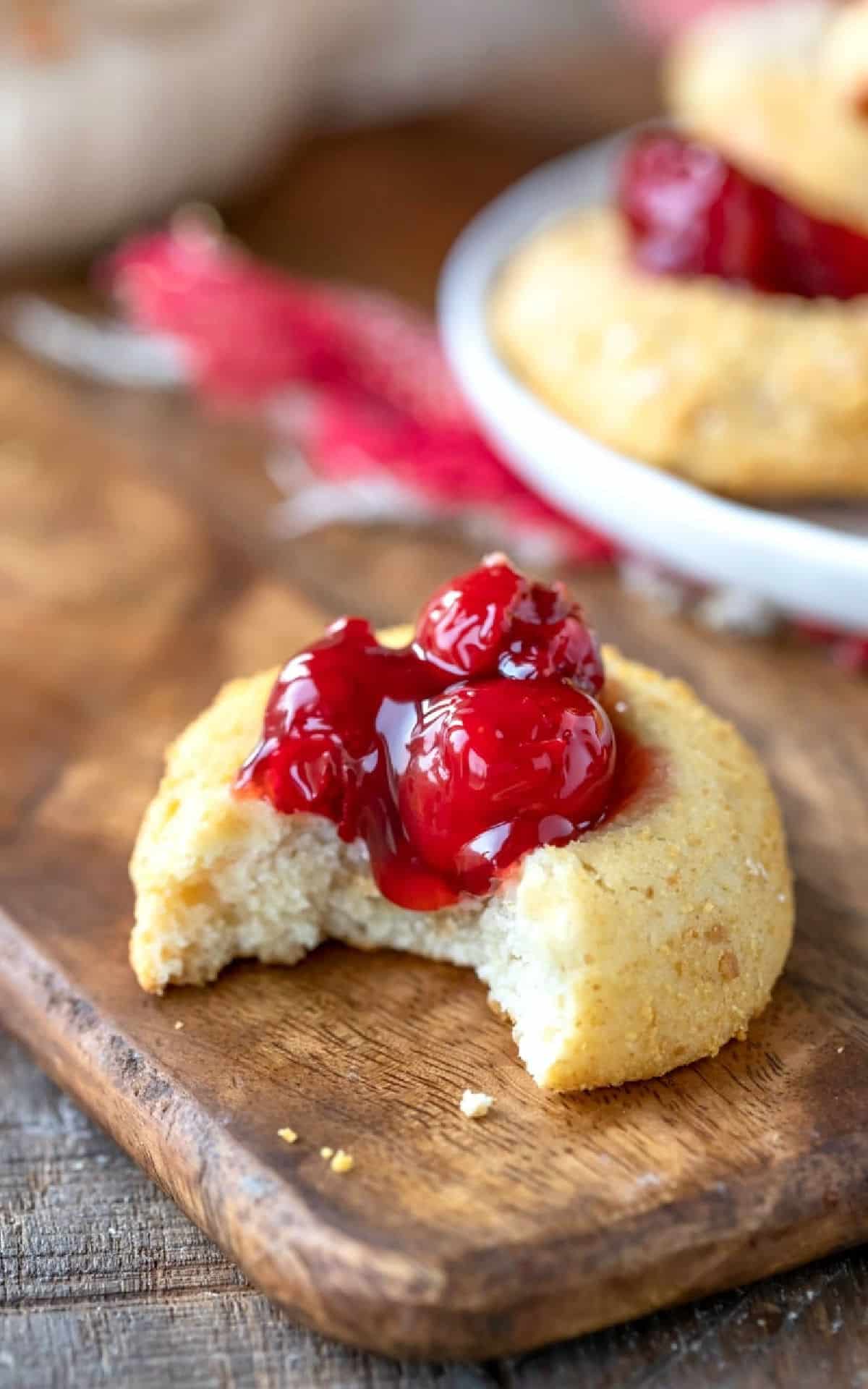 Cherry Cheesecake Thumbprint Cookies Cherry cheesecake thumbprint cookie on a wooden cutting board.