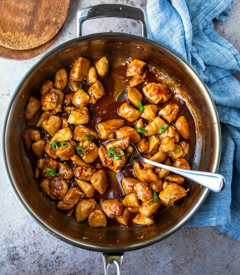 Silver spoon with a scoop of orange chicken.
