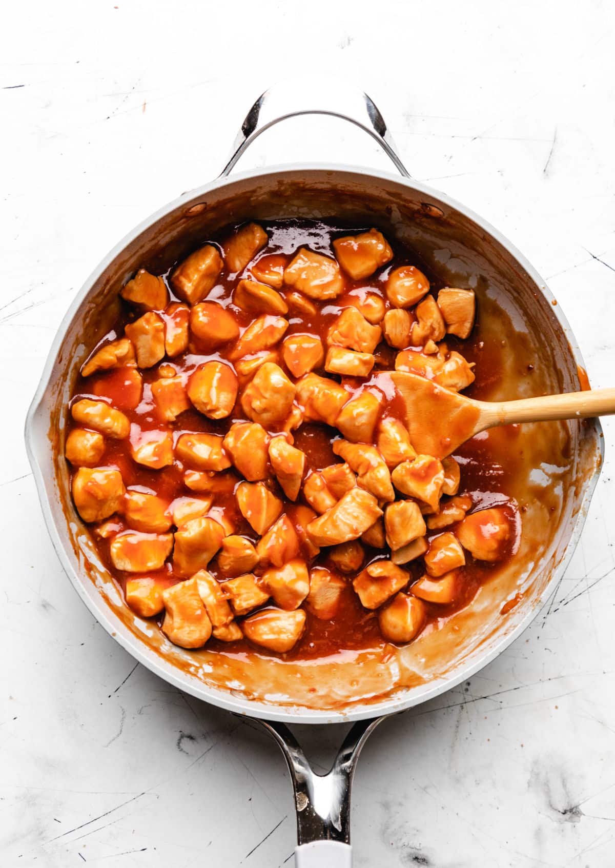 A wooden spoon in a skillet of orange chicken.