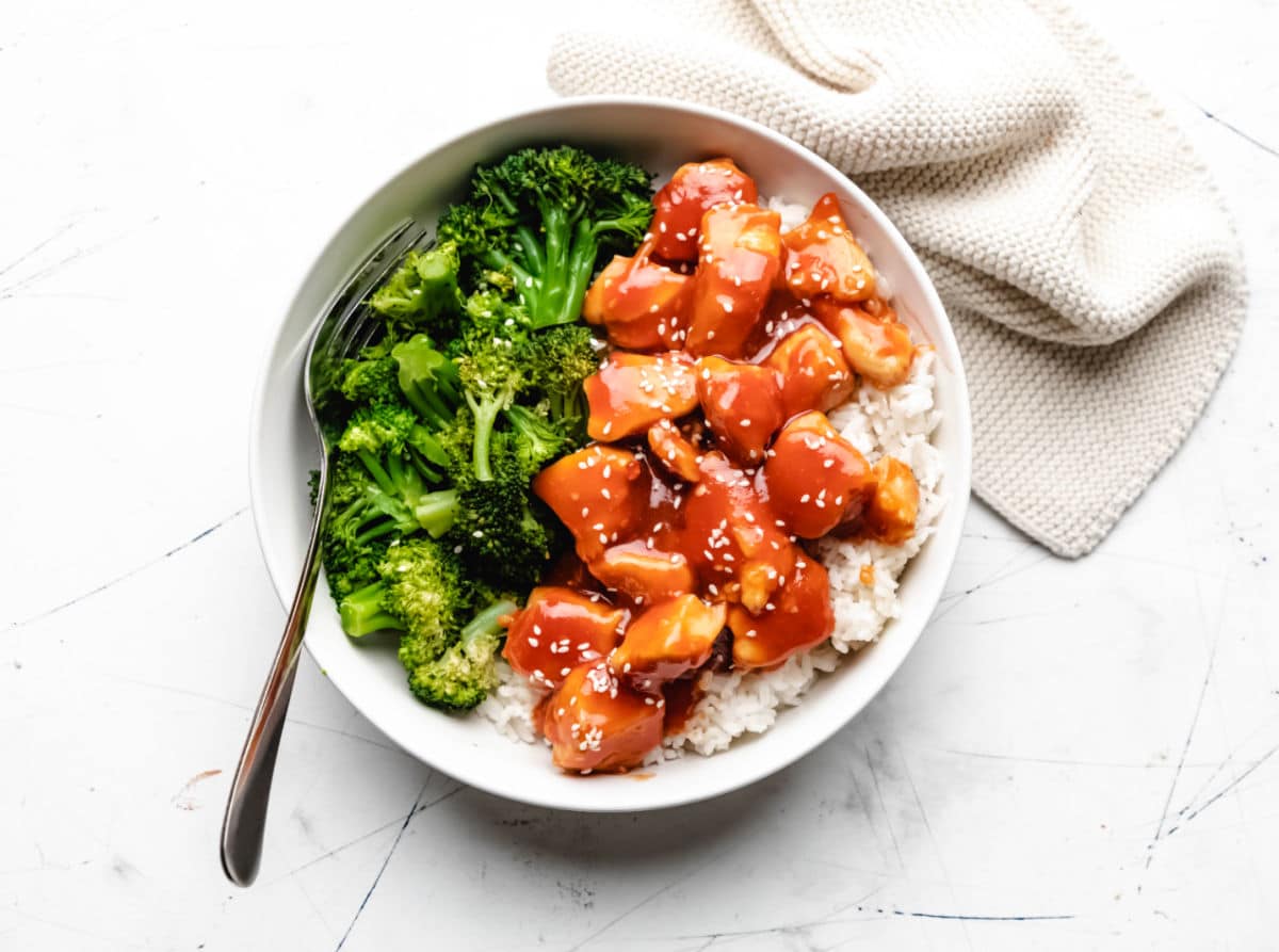 A bowl of orange chicken rice and broccoli with a fork in it. 