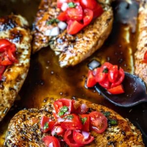 Bruschetta chicken next to a spoon with tomatoes and onion