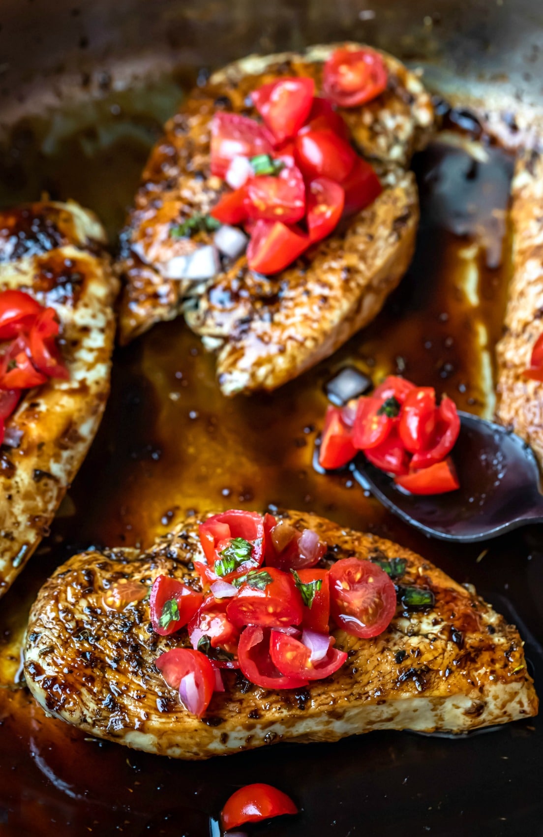 Bruschetta chicken next to a spoon with tomatoes and onion