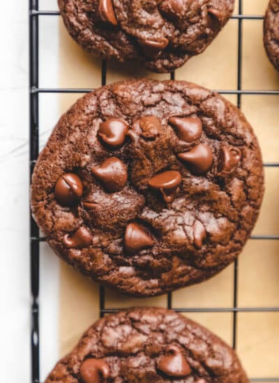 Three chocolate chocolate chip cookies on a black wire cooling rack.