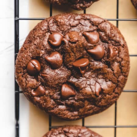 Three chocolate chocolate chip cookies on a black wire cooling rack.