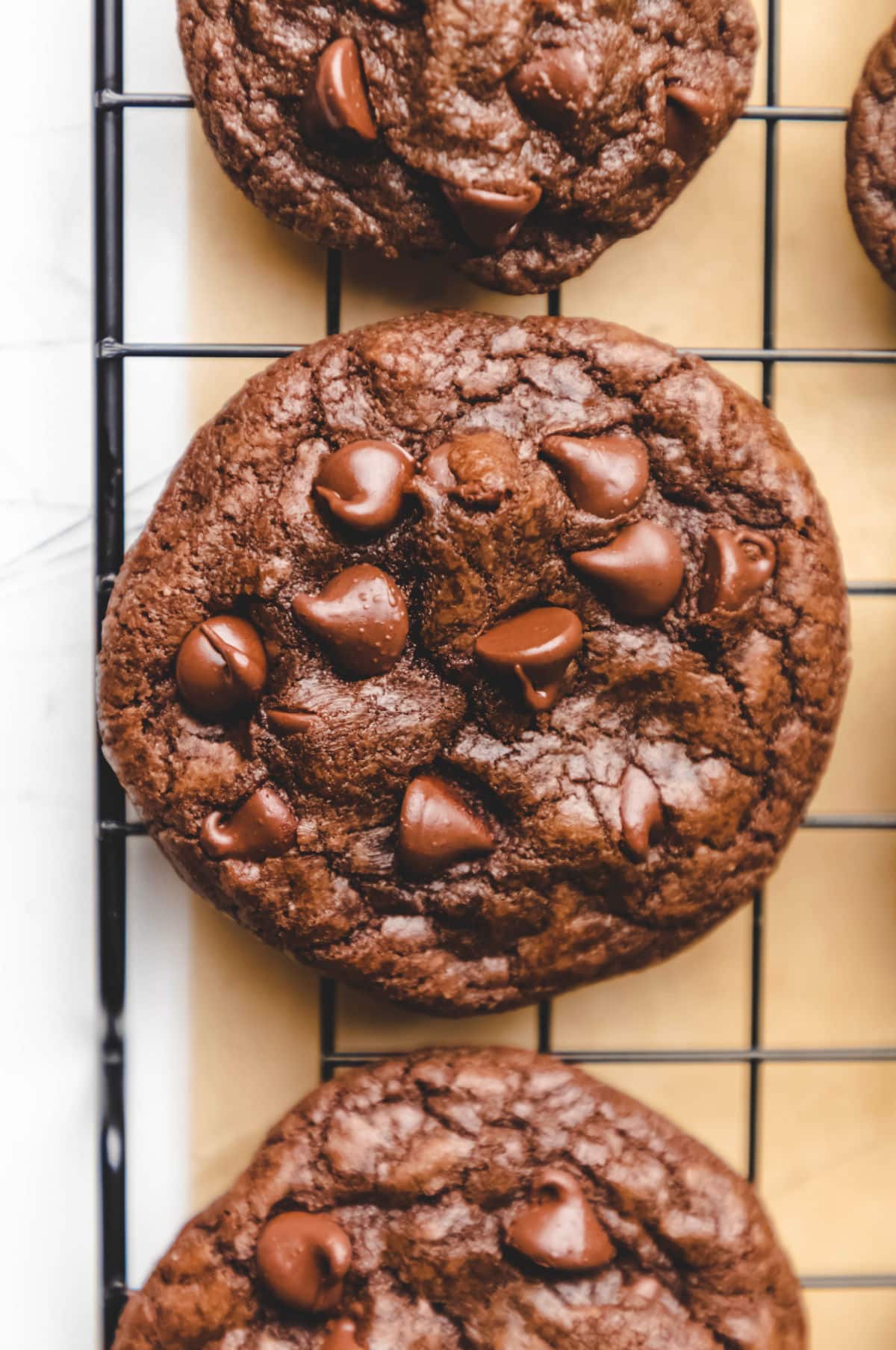 Three chocolate chocolate chip cookies on a black wire cooling rack.