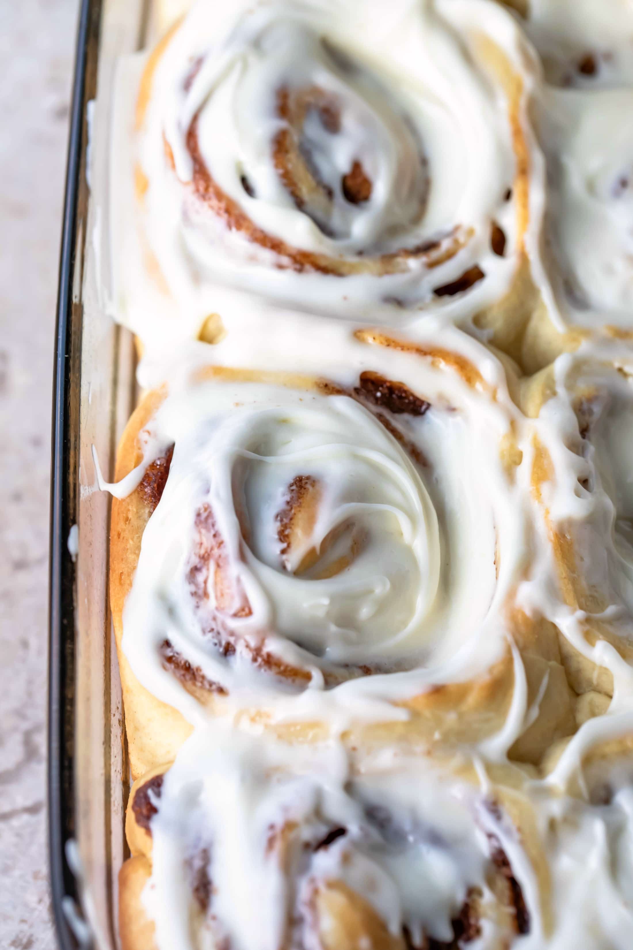 Close up picture of a cream cheese frosted homemade cinnamon roll in a glass pan