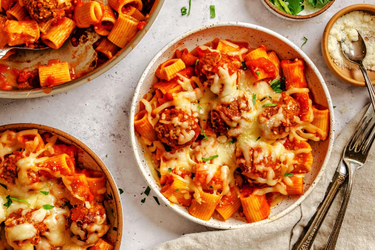 Two plates of meatball pasta next to the skillet.