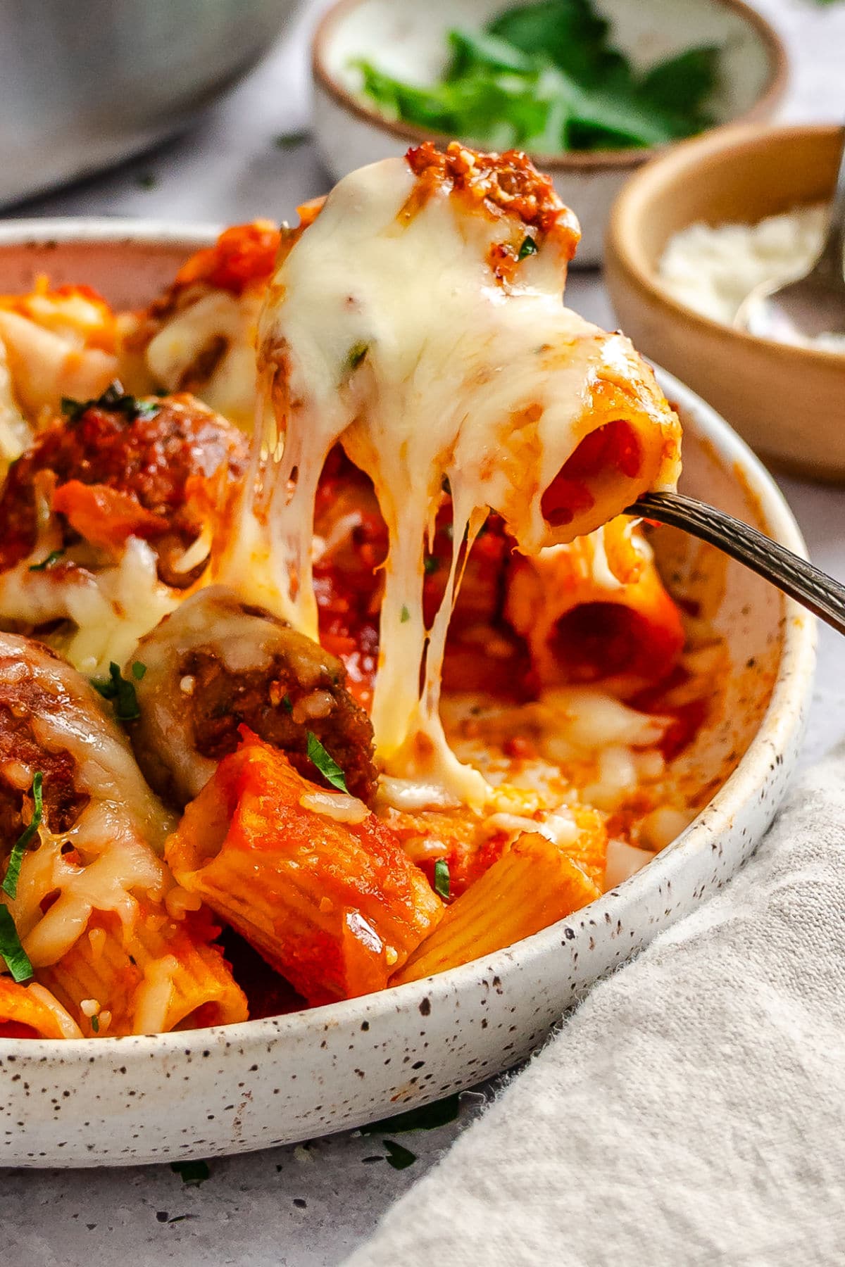 A fork taking a bite of meatball pasta with the cheese pull showing.